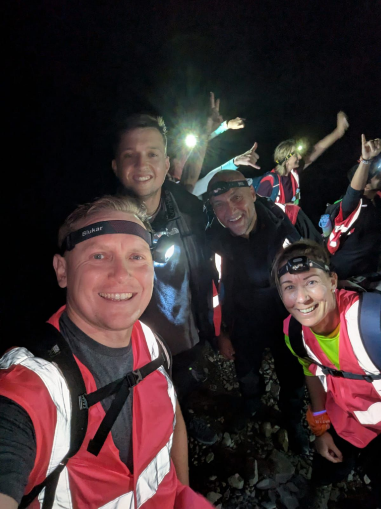 A group of men and women wearing pink high vis jackets and hand touchers. They all look very excited. It is dark.